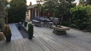 A wooden deck with outdoor furniture, including a sofa and a coffee table, surrounded by greenery and trees. - Cosy House In Lovely Market Town (Newport)