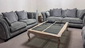 Un salon avec deux canapés gris, une table basse avec un plateau en verre et des coussins décoratifs à motifs.