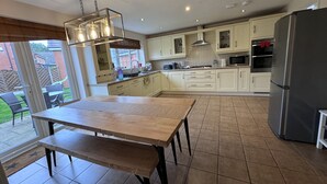 Une cuisine moderne avec des meubles blancs, un réfrigérateur en acier inoxydable et un coin repas comprenant une table et un banc en bois.