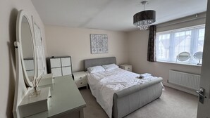 Une chambre à coucher comprenant un lit, des tables de chevet, une commode, un miroir, un lustre et une fenêtre avec des rideaux.