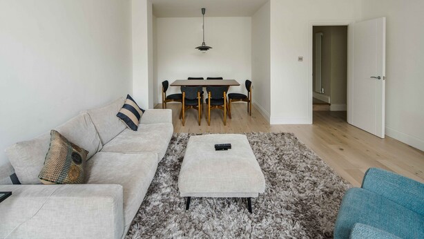 Una sala de estar moderna con un sofá, un reposapiés y una mesa de comedor con sillas.