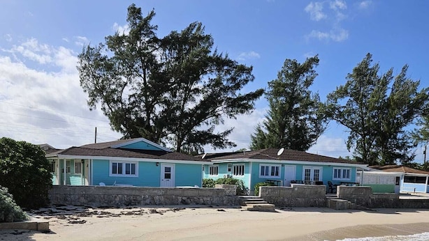 A beachfront property with a two-story building, a sandy beach, and clear turquoise water.