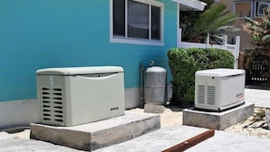 Two air conditioning units placed on a concrete patio in front of a house with a blue exterior.