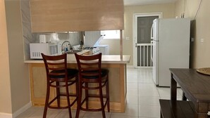 A compact kitchen with a central island, two wooden chairs, a white refrigerator, and a dining table.