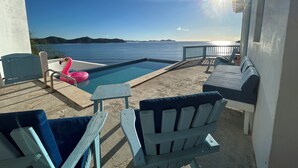 A pool area with a view of the sea, a pink flamingo float, and Adirondack chairs.