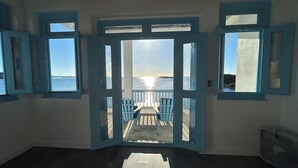 A room with a large open door leading to a balcony with a view of the sea.