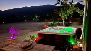 Una mesa de madera con un jacuzzi y plantas en macetas, frente a un paisaje montañoso.