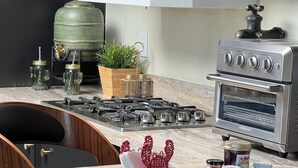 Una cocina con armarios oscuros, estufa a gas, horno empotrado y encimera de mármol.