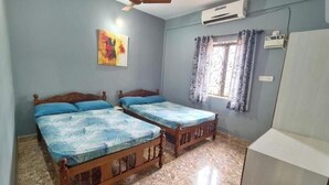 A bedroom with two wooden beds, a ceiling fan, an air conditioner, and a window with curtains. - Jackson's Beach House Calangute  (Calangute)