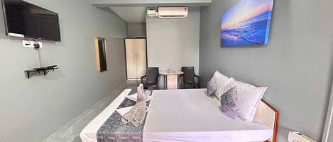 A hotel room with a bed, a flat-screen TV mounted on the wall, a small table with chairs, and a painting on the wall.