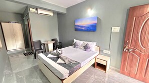 A hotel room with a bed, a desk, a chair, a wardrobe, and a painting on the wall. - Jackson's Beach House Calangute  (Calangute)
