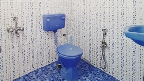 A bathroom with a blue toilet, a shower, and a sink. The walls have a white pattern with blue dots. - Jackson's Beach House Calangute  (Calangute)