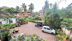 A courtyard with a paved area, parked vehicles, and surrounding greenery. - Jackson's Beach House Calangute  (Calangute)