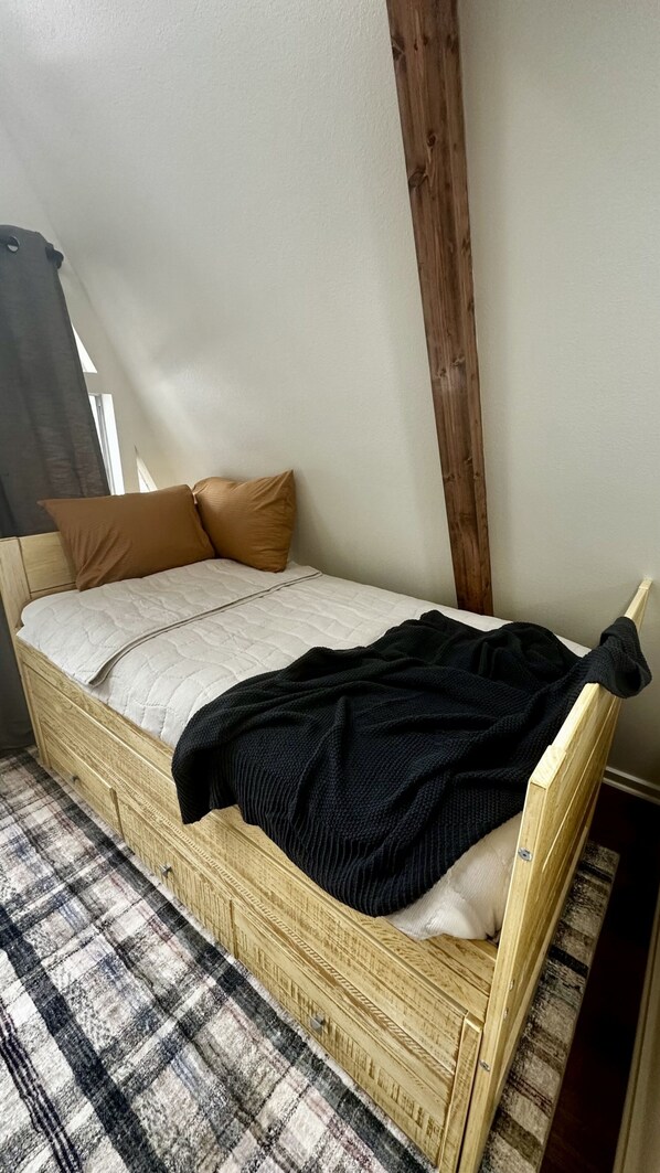 A single bed with a wooden frame, a plaid bedspread, and two pillows.