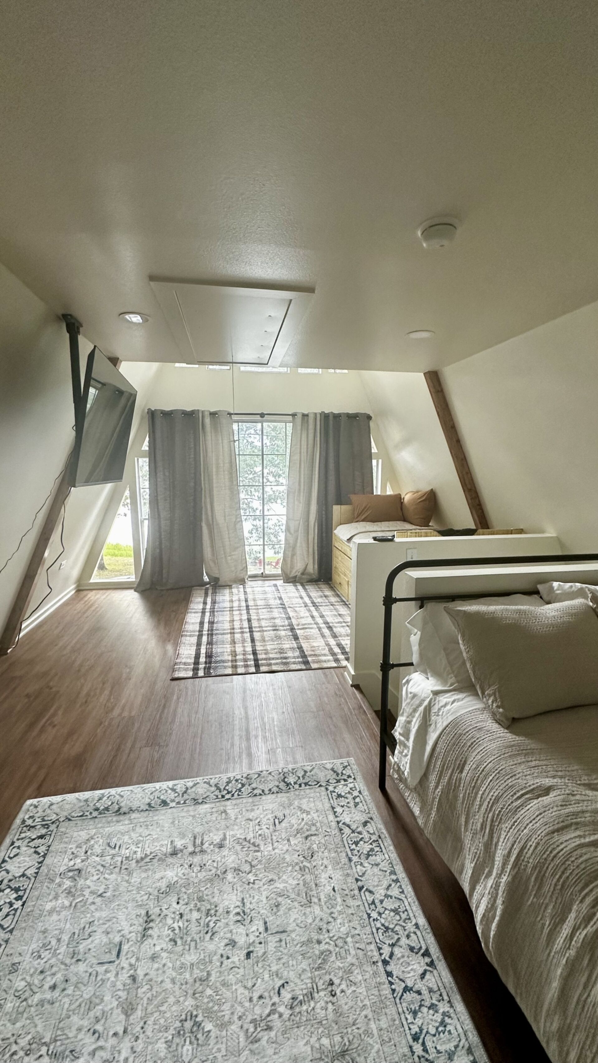 A bedroom with a sloped ceiling, a bed, a bedside table, a window with curtains, and a patterned rug.