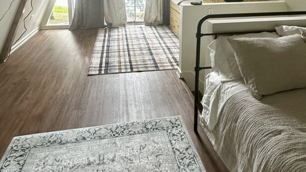 Une chambre à coucher avec un plafond en pente, un lit, une table de chevet, une fenêtre avec des rideaux et un tapis à motifs.