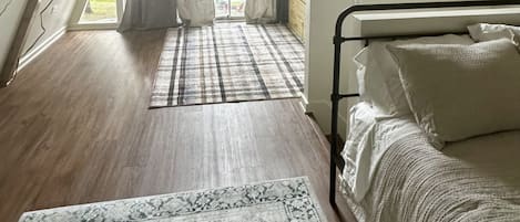 Un dormitorio con techo inclinado, una cama, una mesita de noche, un ventanal con cortinas y una alfombra estampada.