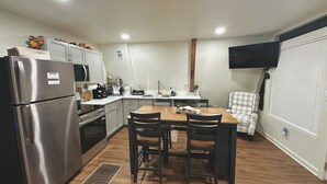 Une cuisine compacte équipée d’un réfrigérateur, d’une cuisinière et d’un four à micro-ondes. On y trouve une table à manger avec quatre chaises. Un téléviseur à écran plat est fixé au mur.