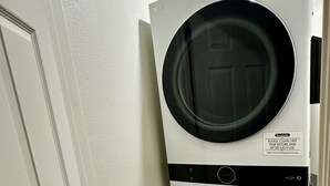 Un appareil compact combinant lave-linge et sèche-linge, à chargement frontal, placé dans un coin d’une pièce dotée d’un plancher en bois et de murs blancs.