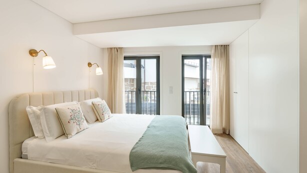 Ein Schlafzimmer mit Bett, Nachttischlampen, einem Fenster mit Vorhängen und Blick ins Freie.