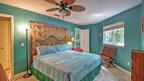 Een slaapkamer met turquoise wanden, een bed met een geborduurd sprei, een plafondventilator, een raam met zonwering en een stoel.