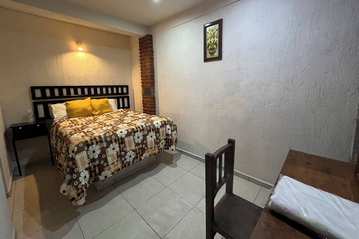 A bedroom with a bed, a nightstand, a chair, and a small table.