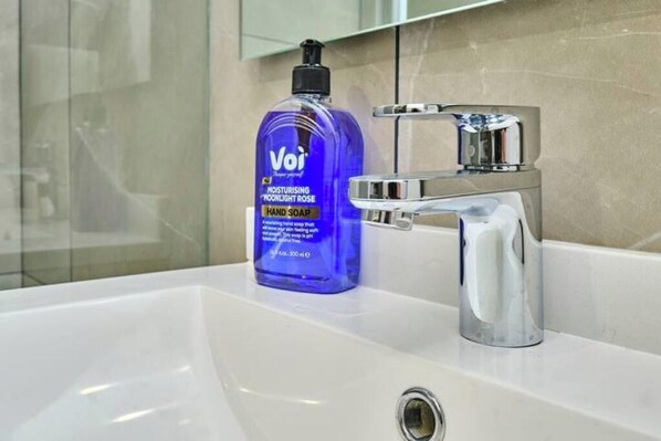 A bathroom sink with a blue bottle of hand soap and a chrome faucet.