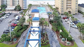 A multi-story hotel with a pool, parking lot, and beach view.