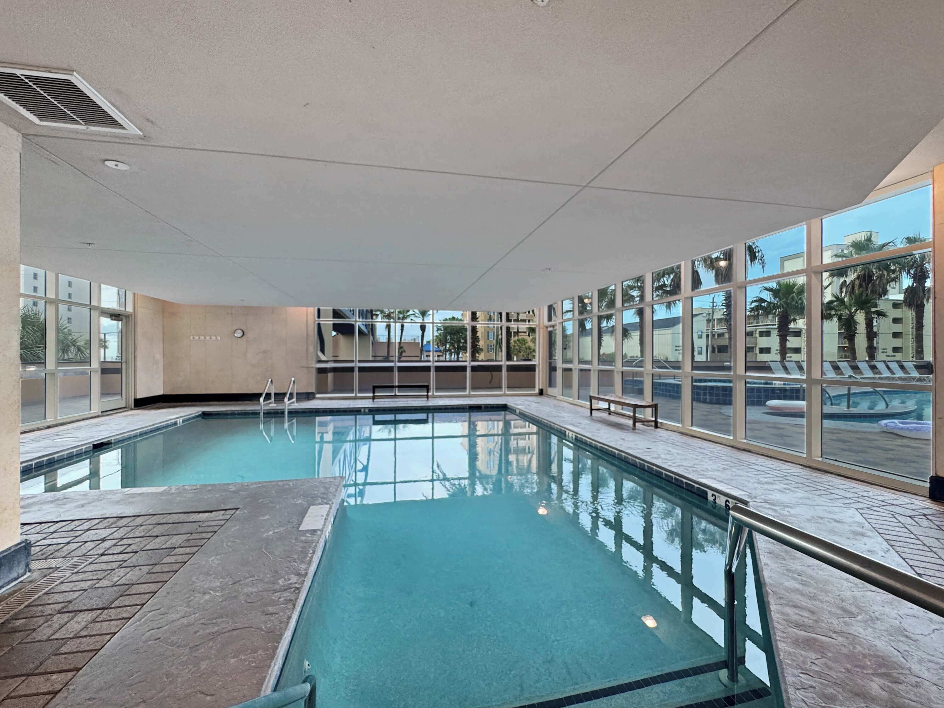 An indoor swimming pool with clear glass walls, a tiled floor, and a bench near the pool.