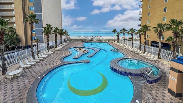 Ein Pool mit kreisförmigem Design, umgeben von Liegestühlen und Palmen, mit Blick auf Strand und Meer im Hintergrund.