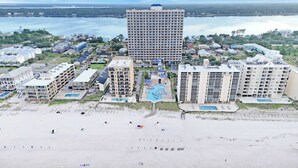 Eine Luftaufnahme eines Küstenresorts mit mehreren Hochhäusern, einem Sandstrand und einem großen Schwimmbad.