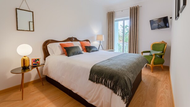 A neatly arranged bedroom with a large bed, bedside tables, a TV, and a chair.