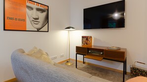A living room with a sofa, a floor lamp, a vintage radio, and a poster on the wall.