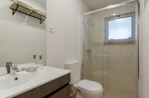 Une salle de bain dotée d’une douche à parois de verre, d’un lavabo blanc avec des accessoires modernes et d’un porte-serviettes placé au-dessus du lavabo.