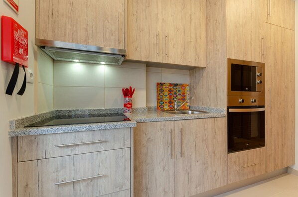 A kitchen with wooden cabinets, a stainless steel range hood, a microwave, and a sink.