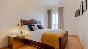 A neatly made bed with a wooden headboard, a bedside table with a lamp, and a window with curtains.