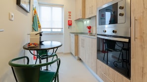 A compact kitchen with wooden cabinets, a stainless steel oven, and a dining area with a table and chairs.