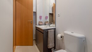 A small bathroom with a wooden door, a sink with a mirror, a toilet, and a towel hanging on the wall. - Setubal Boutique Apartments III by Homing (Setubal)