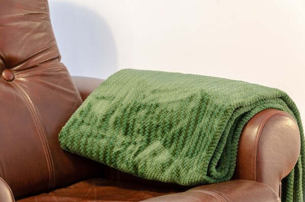 A brown leather armchair with a green knitted throw blanket draped over it.