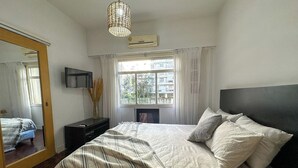 A bedroom with a bed, a mirror, a dresser, a TV, and a window with curtains. - Rent Up-Monoambiente clásico en Recoleta (Buenos Aires)