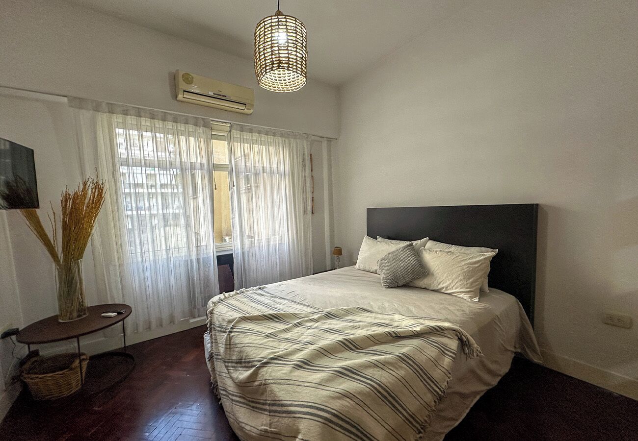 A bedroom with a bed, a bedside table, a lamp, and a window with curtains.