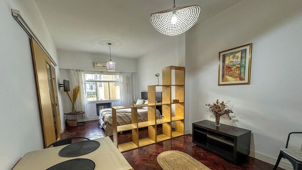 A modern living room with a dining area, a wooden bookshelf, and a TV on a stand. - Rent Up-Monoambiente clásico en Recoleta (Buenos Aires)