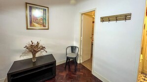 A hallway with a dark wooden console table, a vase with dried flowers, a framed picture on the wall, a chair, and a coat rack. - Rent Up-Monoambiente clásico en Recoleta (Buenos Aires)