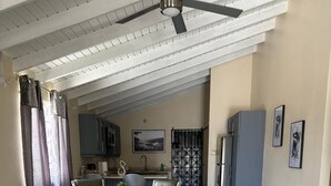 A spacious dining area with a high ceiling and a ceiling fan, leading to a kitchen area with modern appliances and a view of the outdoors. - Sea breeze retreat (Falmouth)