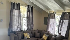 A modern living room with a sectional sofa, a round coffee table, and large windows with curtains. - Sea breeze retreat (Falmouth)