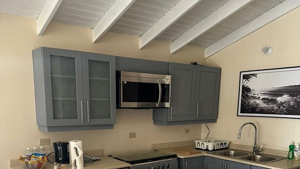 A modern kitchen with grey cabinets, a stainless steel microwave, a gas stove, and a large island with bar stools. - Sea breeze retreat (Falmouth)