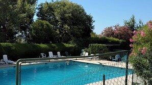 A swimming pool with a chain-link fence, surrounded by white lounge chairs and greenery. - Beautiful 2-bedroom apartment with sea view - swimming pool - tennis court (Villeneuve-Loubet)