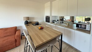 A modern kitchen with white cabinets, a wooden dining table, and a built-in oven. - Beautiful 2-bedroom apartment with sea view - swimming pool - tennis court (Villeneuve-Loubet)
