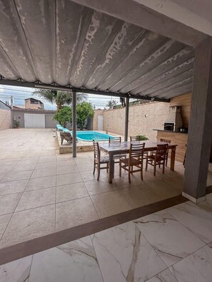 An outdoor patio area with a pool, a dining table with chairs, and a barbecue grill. - Casa Paraíso em Família - Praia Grande (Praia Grande)