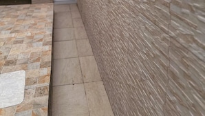 A narrow pathway leading to a garage door, flanked by a textured wall and a tiled floor.